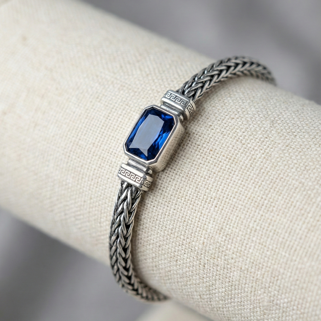 Silver bracelet with a blue gemstone on a white mannequin hand.