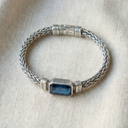 Silver bracelet with a blue gemstone on a beige fabric background