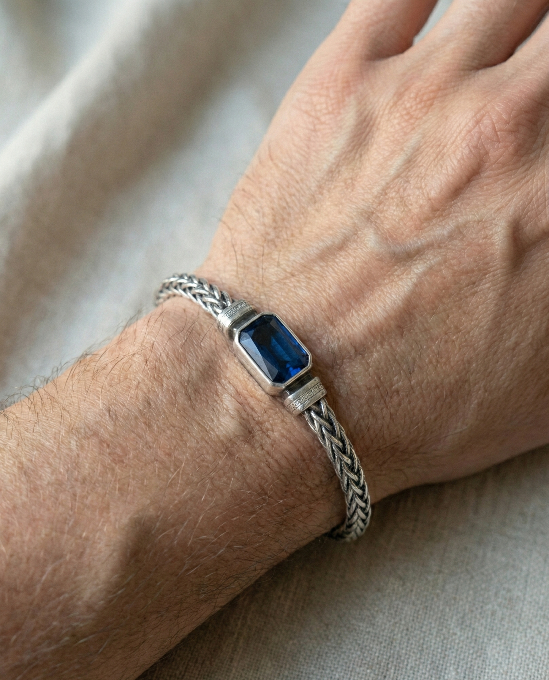 Silver bracelet with a blue stone on a wrist against a neutral background