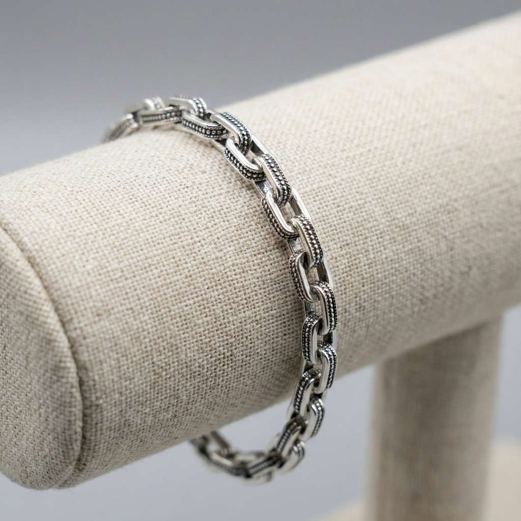 Silver chain bracelet on a beige jewelry stand against a gray background