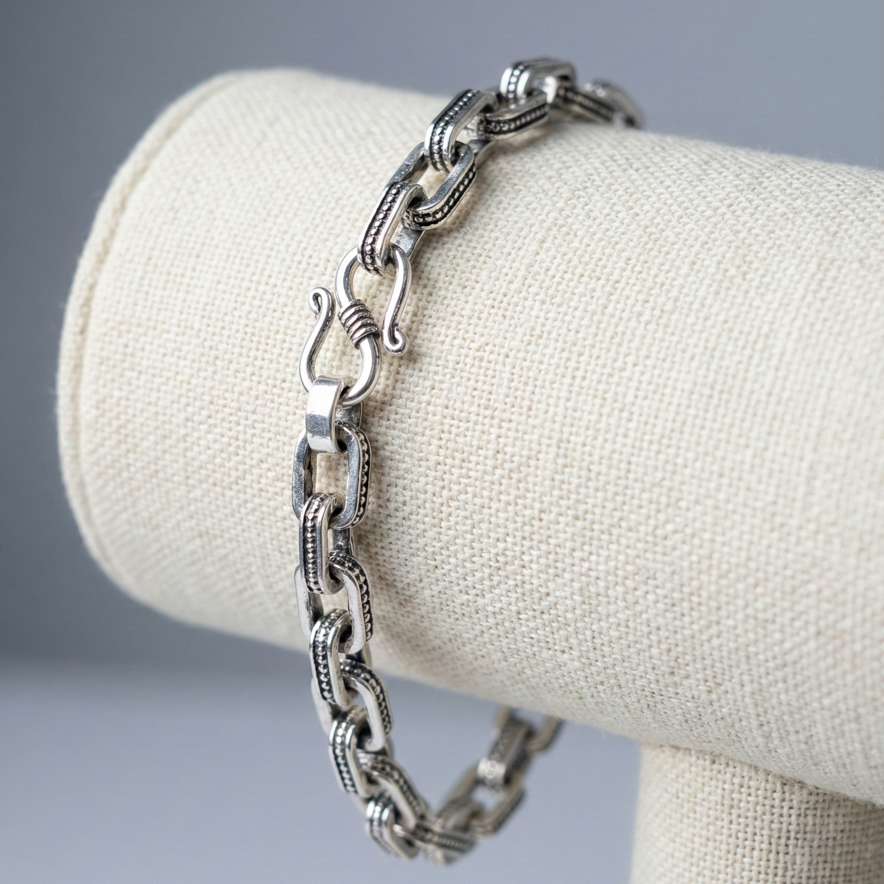 Silver chain bracelet on a white bust against a gray background