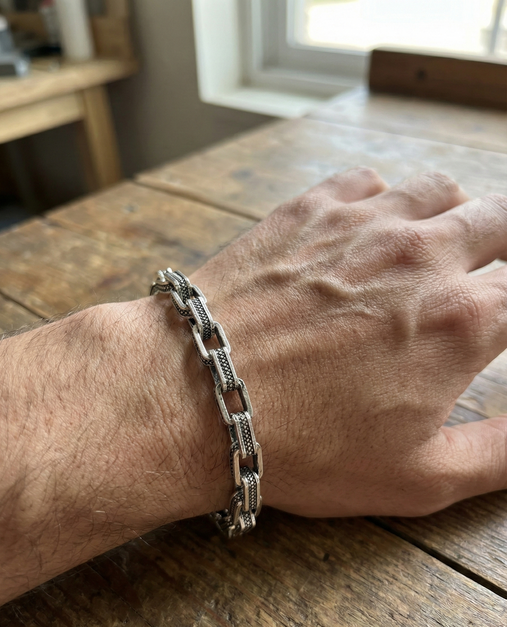 Hand wearing a silver chain bracelet on a wooden surface