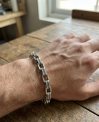 Hand wearing a silver chain bracelet on a wooden surface