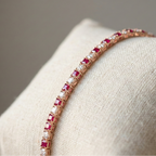 Rose gold bracelet with red gemstones on a beige cushion
